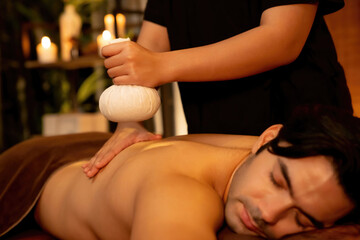 Hot herbal ball spa massage body treatment, masseur gently compresses herb bag on man body....