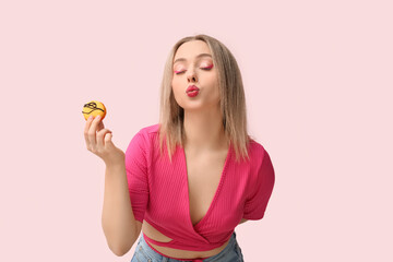 Beautiful young woman with orange sweet macaroon on pink background