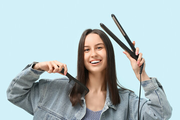 Obraz premium Beautiful young woman with hair straightener and comb on blue background