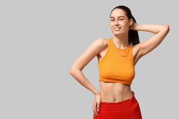 Beautiful young happy woman with piercing navel on grey background