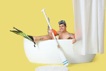 Young man with flippers and paddle in bathtub on yellow background © Pixel-Shot