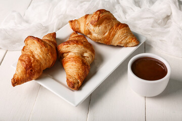 Plate with tasty croissants and bowl of jam on white wooden background