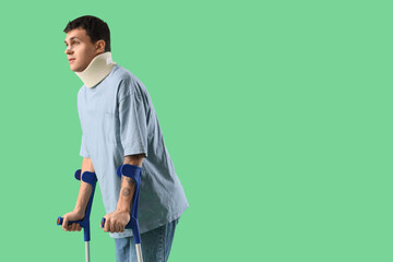 Fototapeta premium Injured young man after accident with crutches on green background