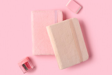 Notebooks, rubber and pencil sharpener on pink background