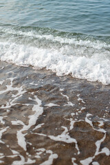 Small foamy waves come and go on a sandy beach by the sea at sunset, a pleasant vacation on summer vacation, relaxation, a walk on the water to the sound of the surf, high quality vertical photo