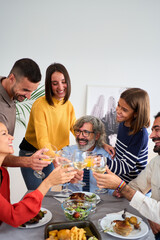 Vertical. Happy Caucasian people toasting with white wine at a meal at home. Smiling family of diverse generations together around the table at festive event at weekend. Domestic life celebration 