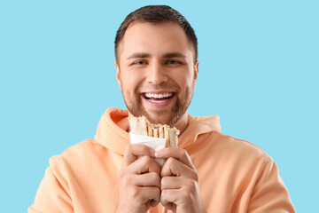 Happy young man with tasty doner kebab on blue background