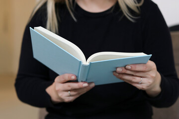 Obraz premium Close up portrait of a woman sitting on a couch and holding a blue mockup book. Education, reading and studying concept 