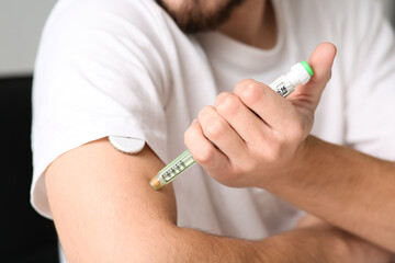 Diabetic young man using lancet pen at home, closeup