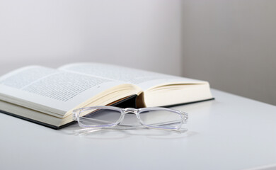 Close up of transparent glasses and an open book on white table 
