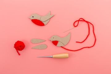  a craft project in progress, cardboard bird in light brown with red yarn belly, black stitched...