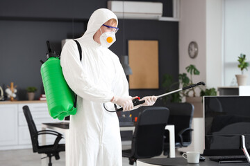Male worker wearing hazmat suit with disinfectant cylinder in office