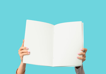 Female hands with open blank magazine on blue background