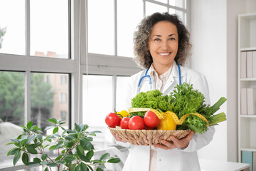 Mature female nutritionist with healthy vegetables and tape measure in office