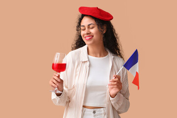 Beautiful young happy African-American woman with flag of France and glass of red wine on beige background