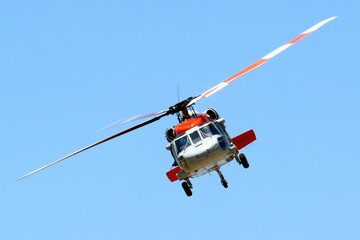 Red and white helicopter flying in a clear blue sky
