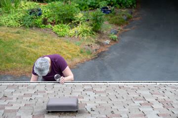 Middle aged white woman with gray installing a downspout filter in a roof rain gutter, perspective from above
