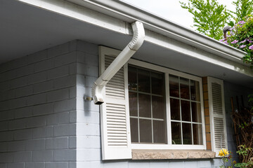 Homeowner maintenance, sections of rain gutter downspout removed for cleaning out, exterior of light gray house with window and white shutters
