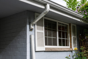 Homeowner maintenance, sections of rain gutter downspout removed for cleaning out, exterior of light gray house with window and white shutters
