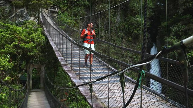 Latin Traveler with Backpack Crossing Wooden Bridge in Front of Pail&oacute;n del Diablo Waterfall, Ecuador