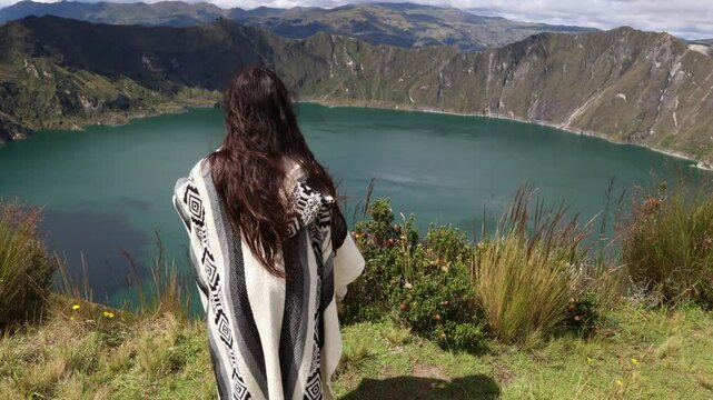 young latin woman in poncho gazes at blue lagoon inside Quilotoa volcano (3,914 m)