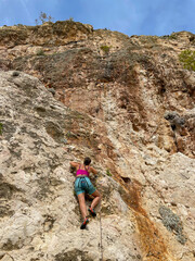 LOW ANGLE VIEW: Young athletic woman lead climbing at beautiful Croatian seaside
