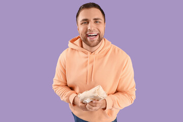 Happy young man with tasty doner kebab on lilac background