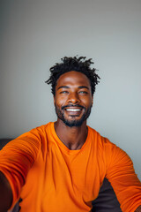 Fototapeta premium A young man in an orange shirt smiling and taking a selfie. Generated by AI.