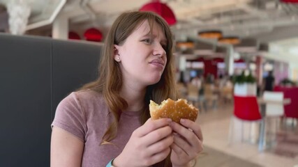 Sad depressed young woman eating burger in fast food restaurant. Eating disorder concept. 
