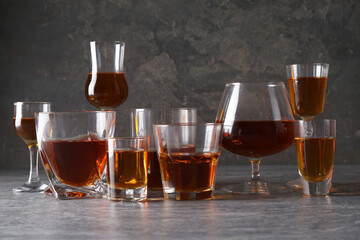 Many different liqueurs in glasses on grey textured table
