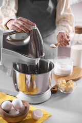 Woman adding sugar into bowl of stand mixer while making dough at table indoors, closeup