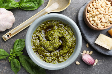 Tasty pesto sauce in bowl, basil, pine nuts, cheese and garlic on grey table, flat lay