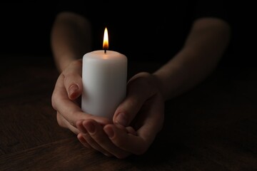 Woman holding burning candle at wooden table, closeup