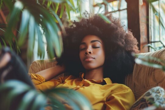 Young black woman with natural hair enjoys a peaceful moment, resting on a comfortable sofa amidst lush green plants