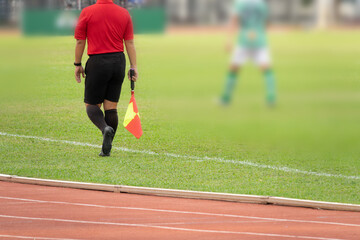 A referee is walking on a track with a yellow and red flag in his hand