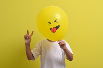 Tongue emoji. Cute Asian boy hiding his face behind balloon emoticon sticking out tongue isolated...