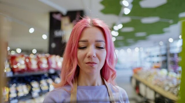 close up of a happy girl with pink hair a supermarket worker lays out goods on the counter. A girl supermarket worker lays out goods on the shelves