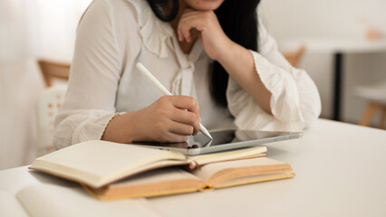 cropped shot, Young Asian female in casual clothes using stylus pen, drawing on her digital tablet at her desk