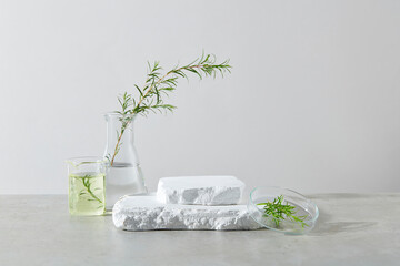 An empty podium of two plaster pedestals placed on each other in the center, on both sides decorated by a few laboratory glassware contain tea tree plants in. Space for product displaying, front view