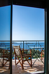 Holiday concept picture with a chair on a balcony facing out to a blue sea and sky. Vacation and travel image.