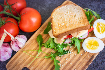 Toast with fish, cheese, arugula, salad, cucumbers, radish, and pepper on a cutting board, with eggs and vegetables. Healthy food.