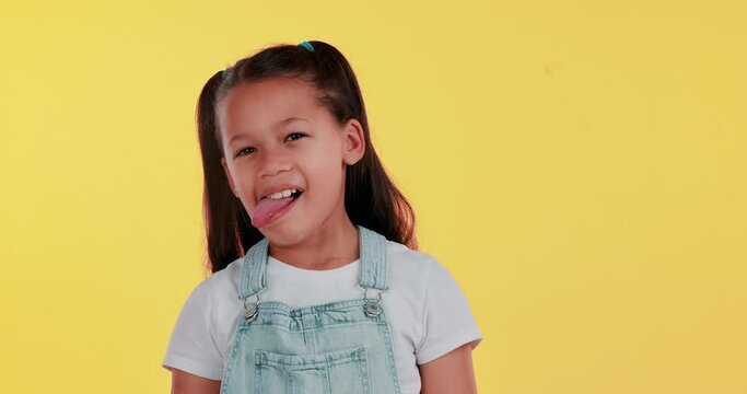 Funny, face and child in studio with tongue out for playful gesture, positive attitude and happy development. Playing, comedy and portrait of crazy girl with silly games, fun and yellow background
