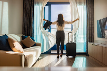 Attractive businesswoman with suitcase opening curtains, looking at the view from window of Beautiful panoramic tropical seascape horizon. Peace sunset sky, relax. Positive energy, meditation, island.