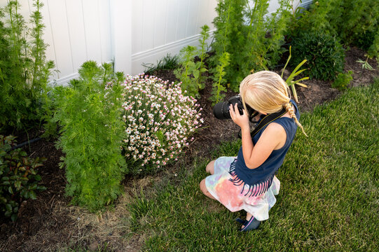Child photographing flowers with a DSLR camera in a garden