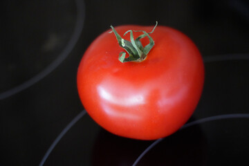 Red tomato on a black ceramic hob in the kitchen