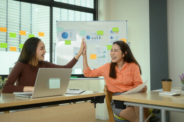 Cheerful young businesswomen giving high five each other celebrating their achievement in office