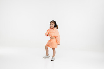 Happy little girl in bright clothes and wireless headphones dances and enjoys music on a white background. demonstrates different positive emotions of the child. Isolated, on white