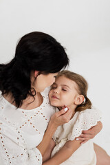 Family relationship between mother and daughter. Loving mother with her little daughter on a light studio background. Tender moment, family support.