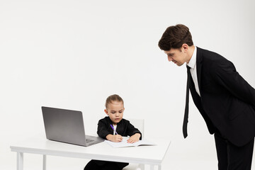 A business little girl in a stylish formal suit signs documents at her desk against a light background. Concept of business, finance and children's emotions.