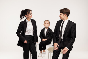 family dressed in classic black suits and white shirts, standing and sitting against the backdrop...